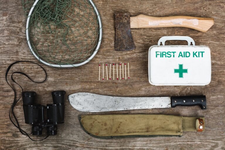 Flat lay of survival equipment including compass, rope, knife, canteen, and map arranged on a rustic wooden surface.